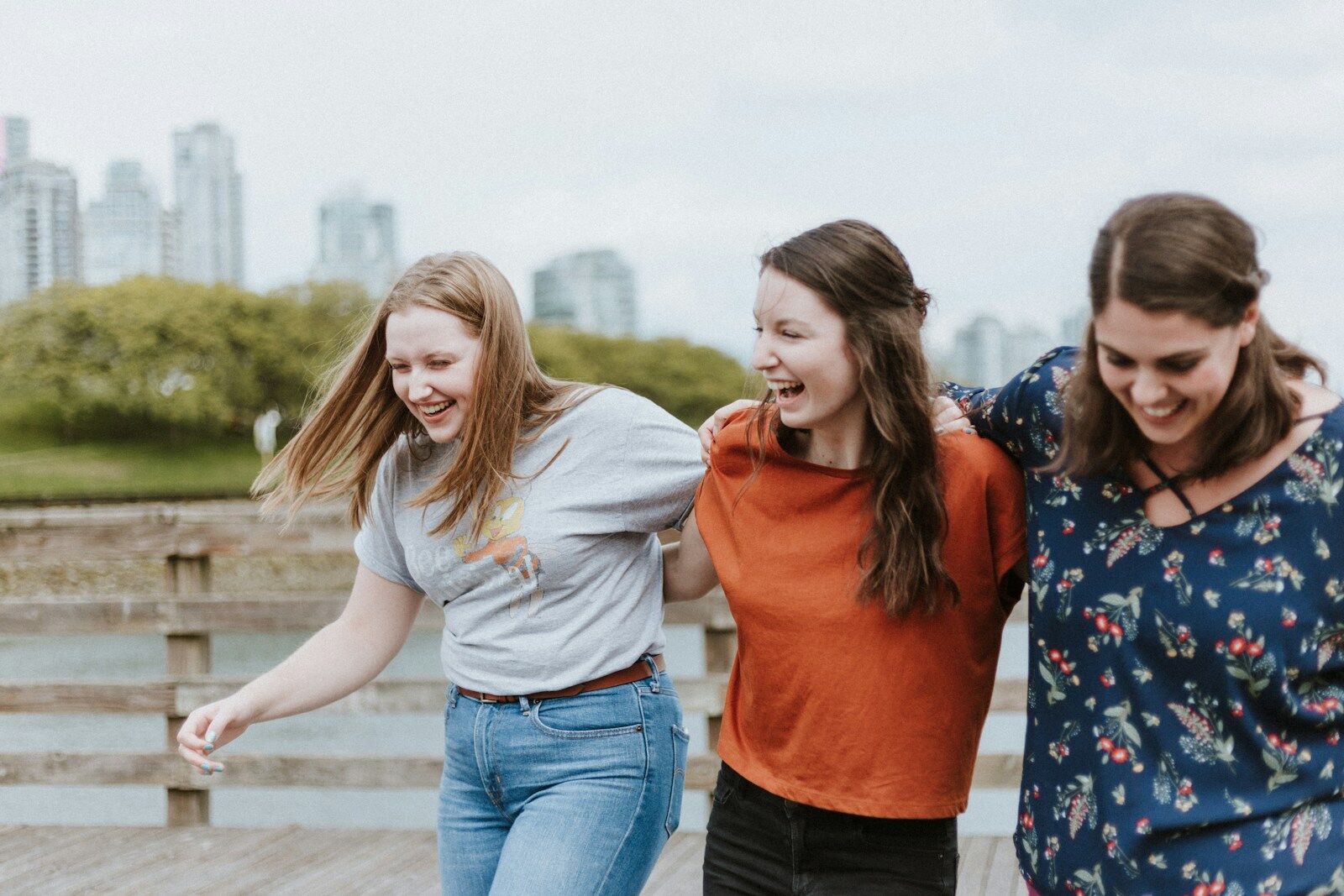 three women walking on brown wooden dock near high rise building during daytime, participating in the levels of intimacy