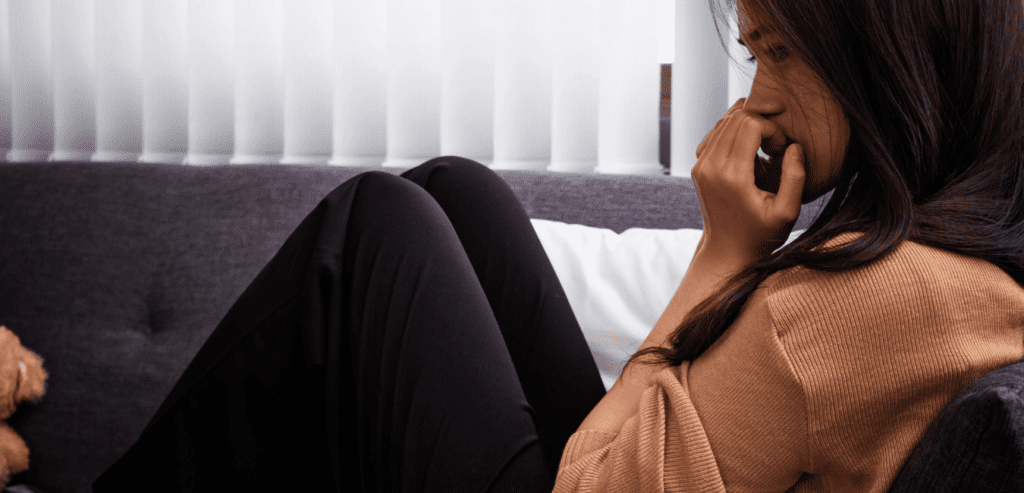 A stressed woman sitting on sofa with her hands on her face while to somewhere and seems thinking some negative thoughts
